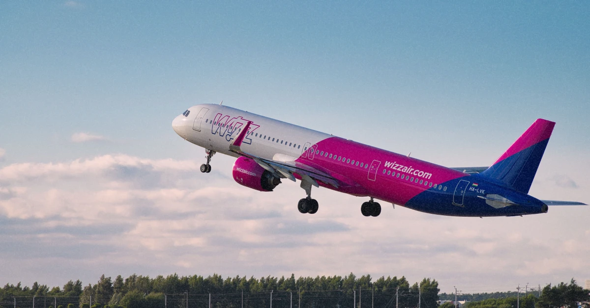 Яскравий рожево-білий літак Wizz Air піднімається в небо у сонячний літній день